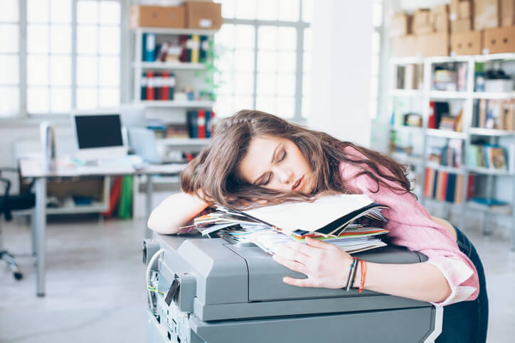Tired and exhausted young woman sleeping on printer in the office.